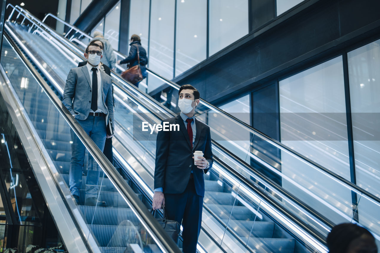 Business people moving down on escalator during pandemic
