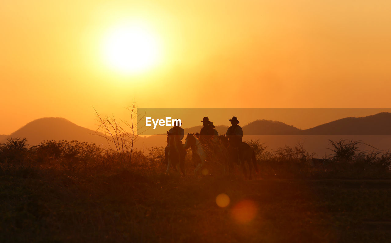 SILHOUETTE PEOPLE ON FIELD AGAINST ORANGE SKY DURING SUNSET