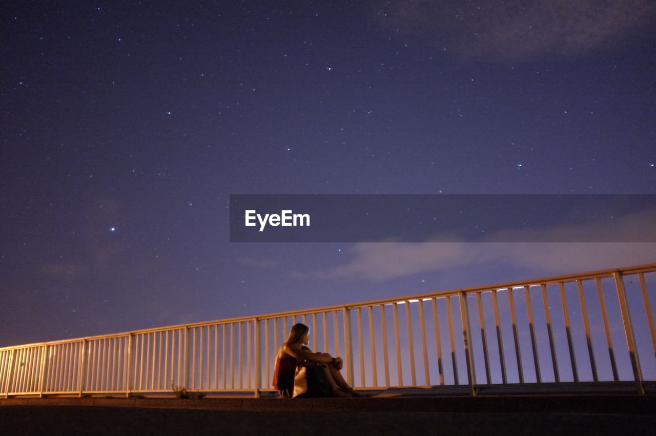 Young woman sitting on bridge at night