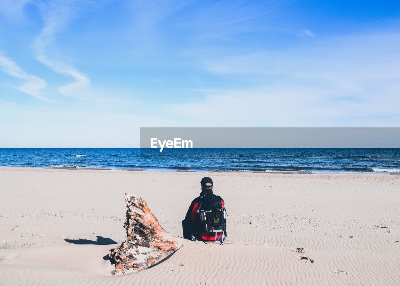 Man sitting at beach against sky during sunny day