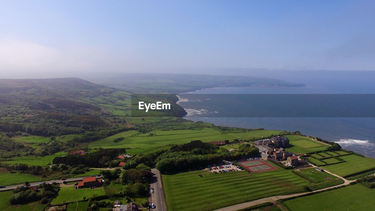 Aerial view of green landscape by sea against sky