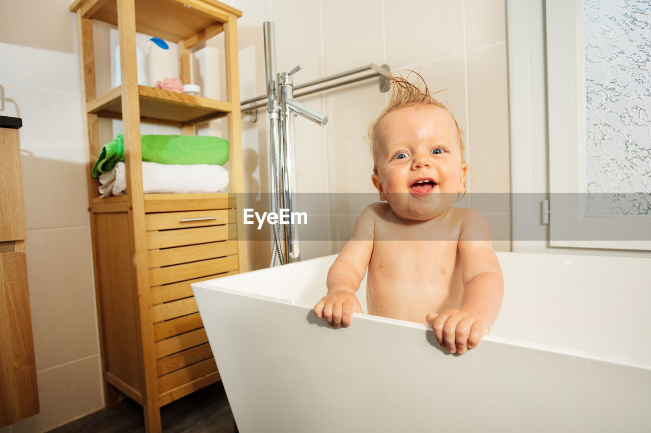 portrait of cute baby boy sitting in bathtub at home