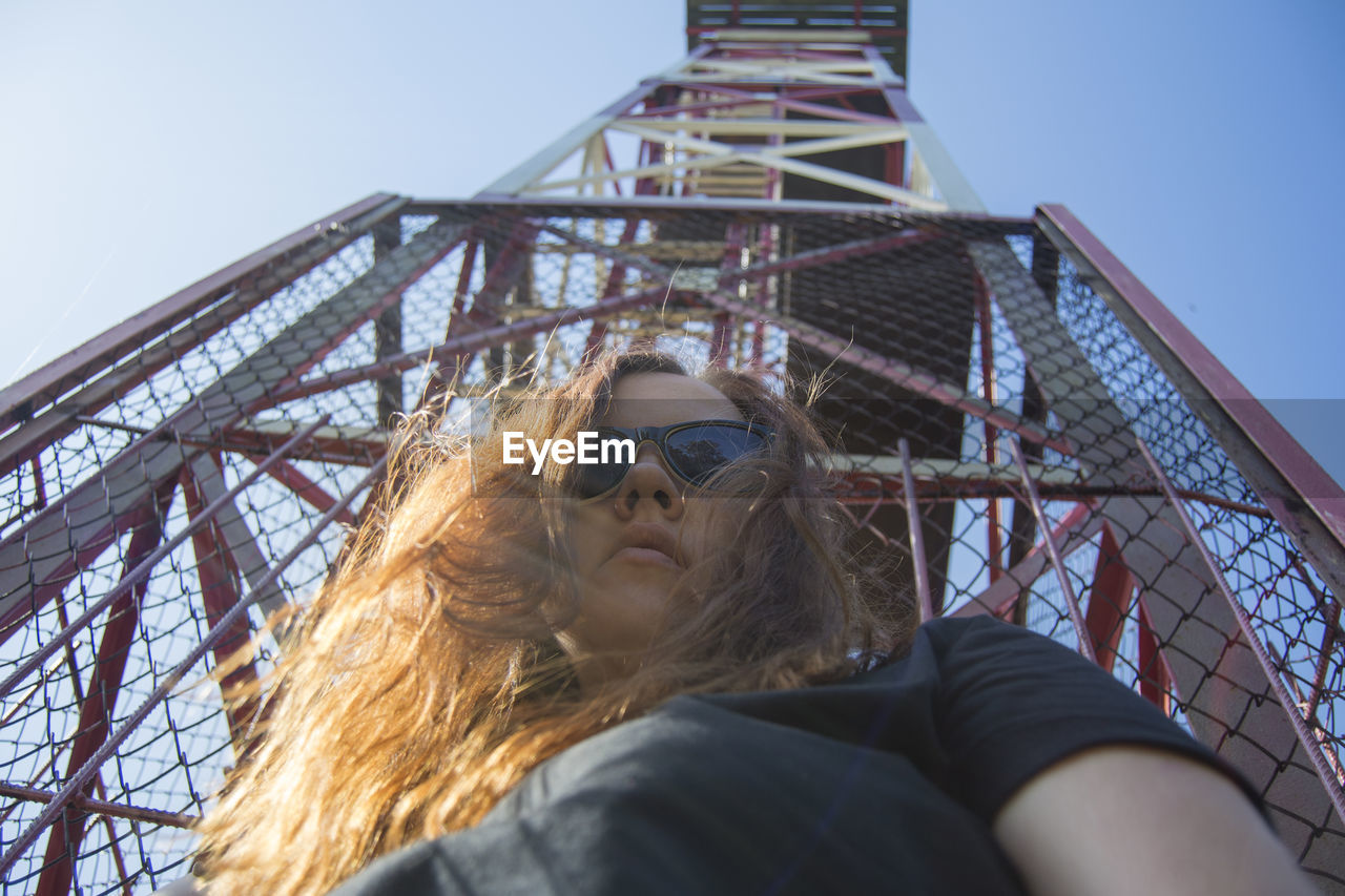 Low angle view of mid adult woman wearing sunglasses standing against tower