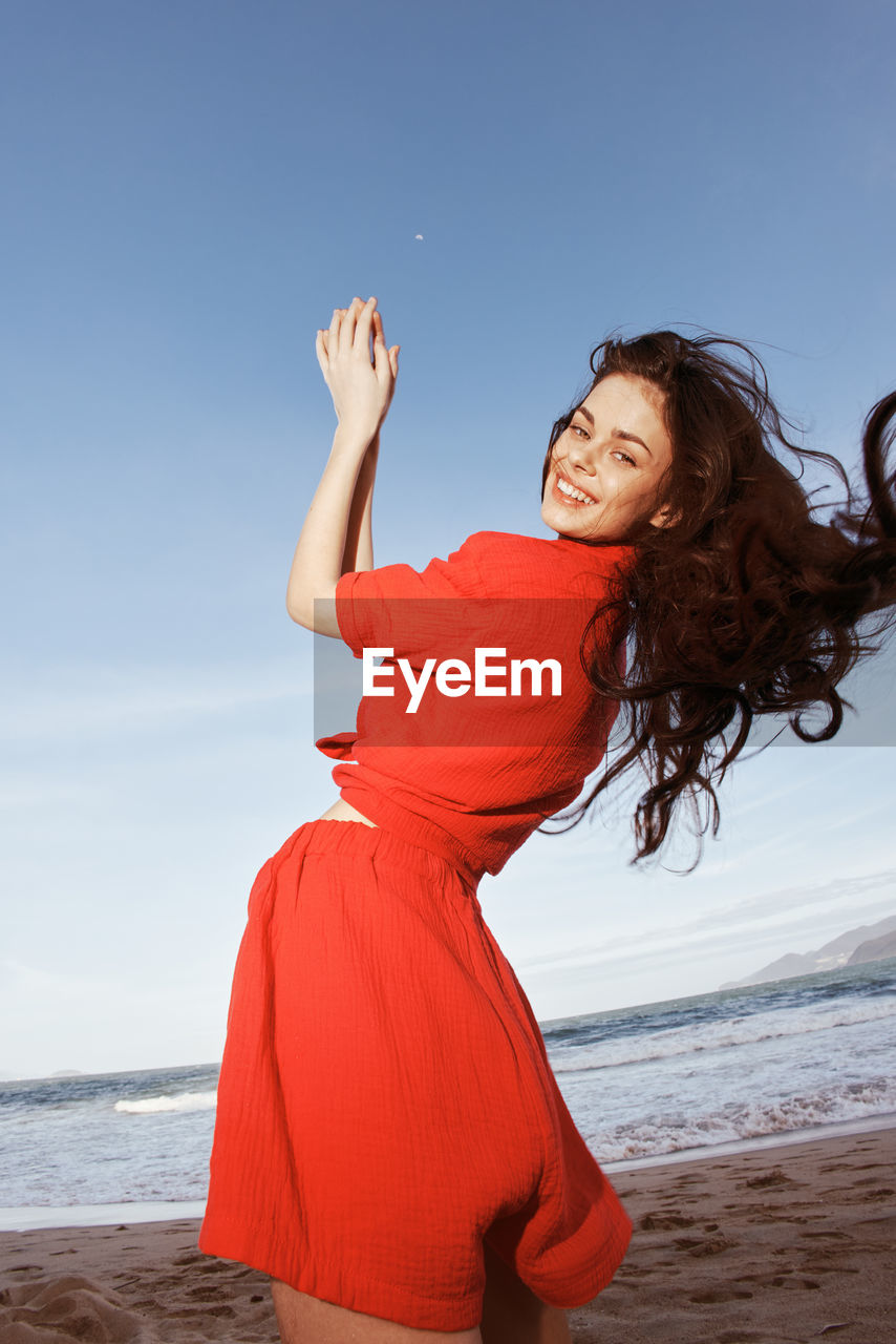 rear view of young woman standing at beach against clear sky