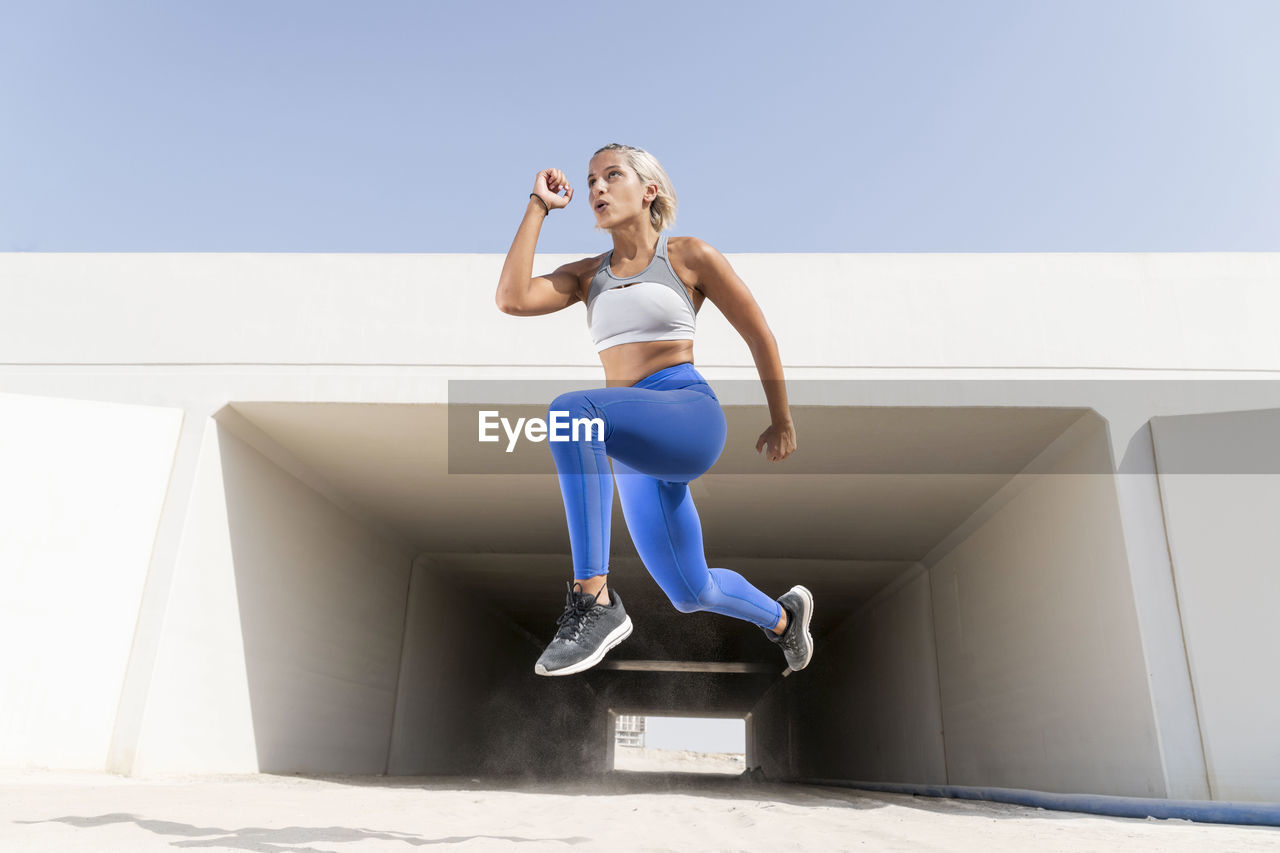 Young woman exercising by built structure against sky