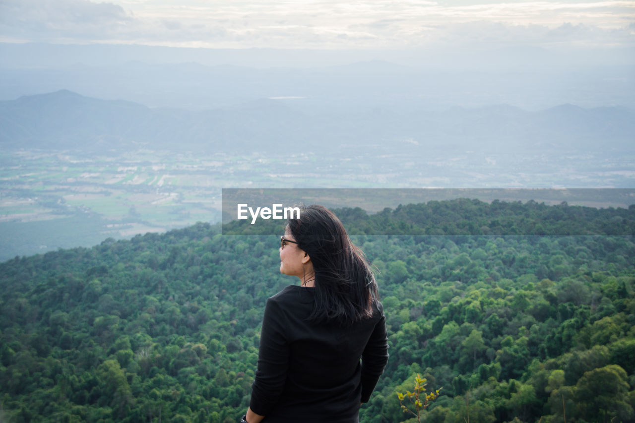 Rear view of woman looking away while standing against mountain landscape