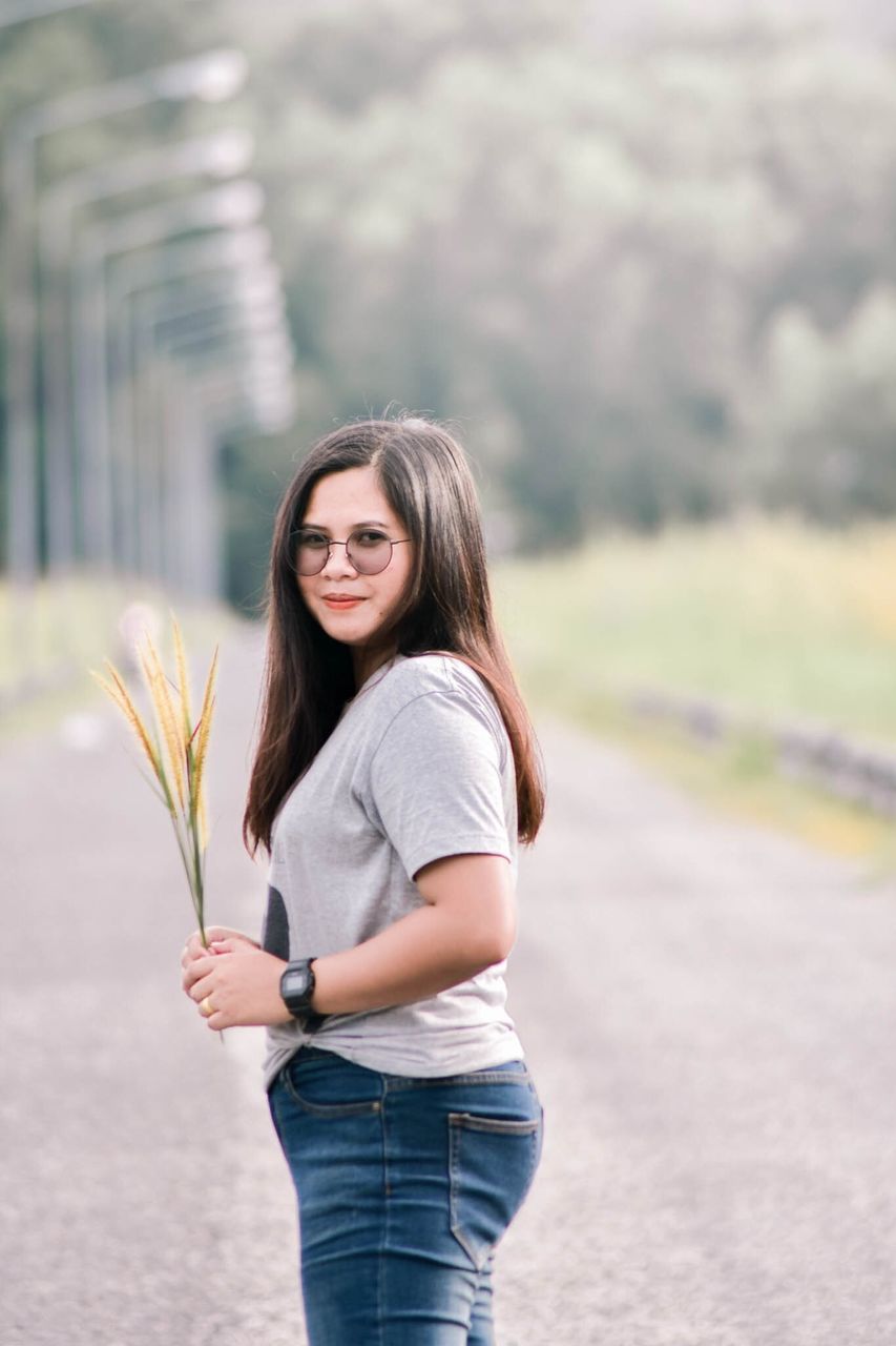 Portrait of beautiful young woman with plant standing on road 