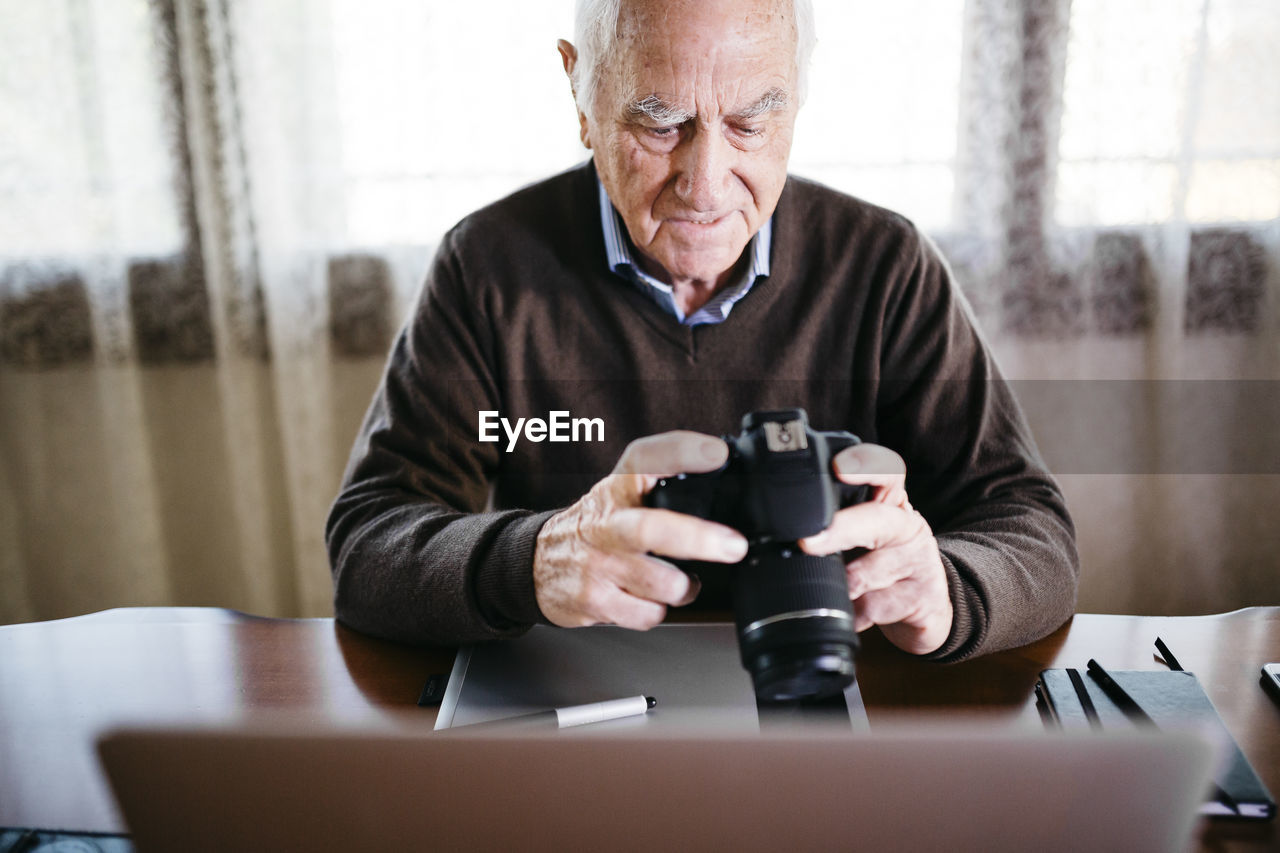 Senior photographer with laptop and digital camera at home