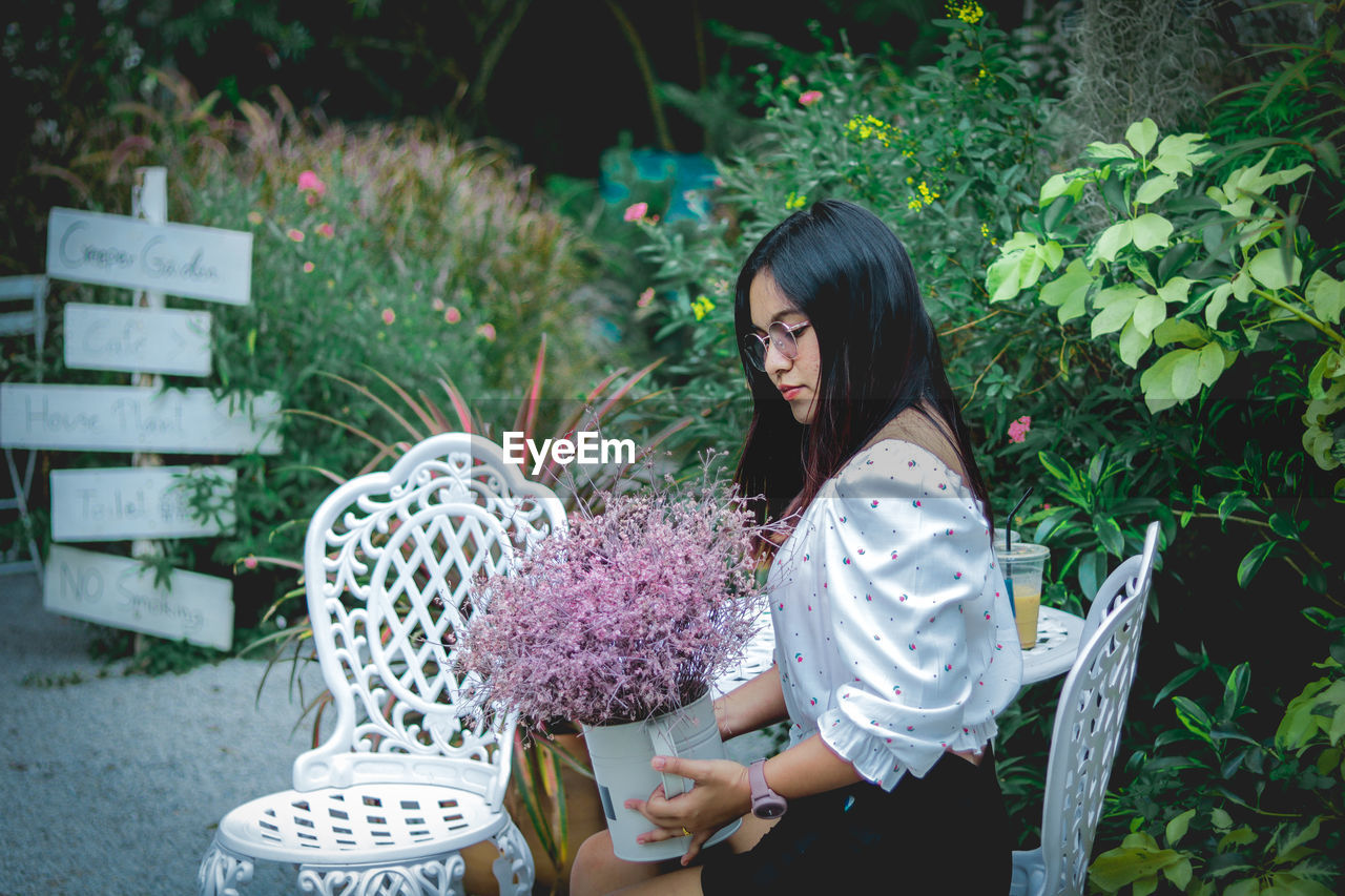 Young woman holding flowers in standing by plants