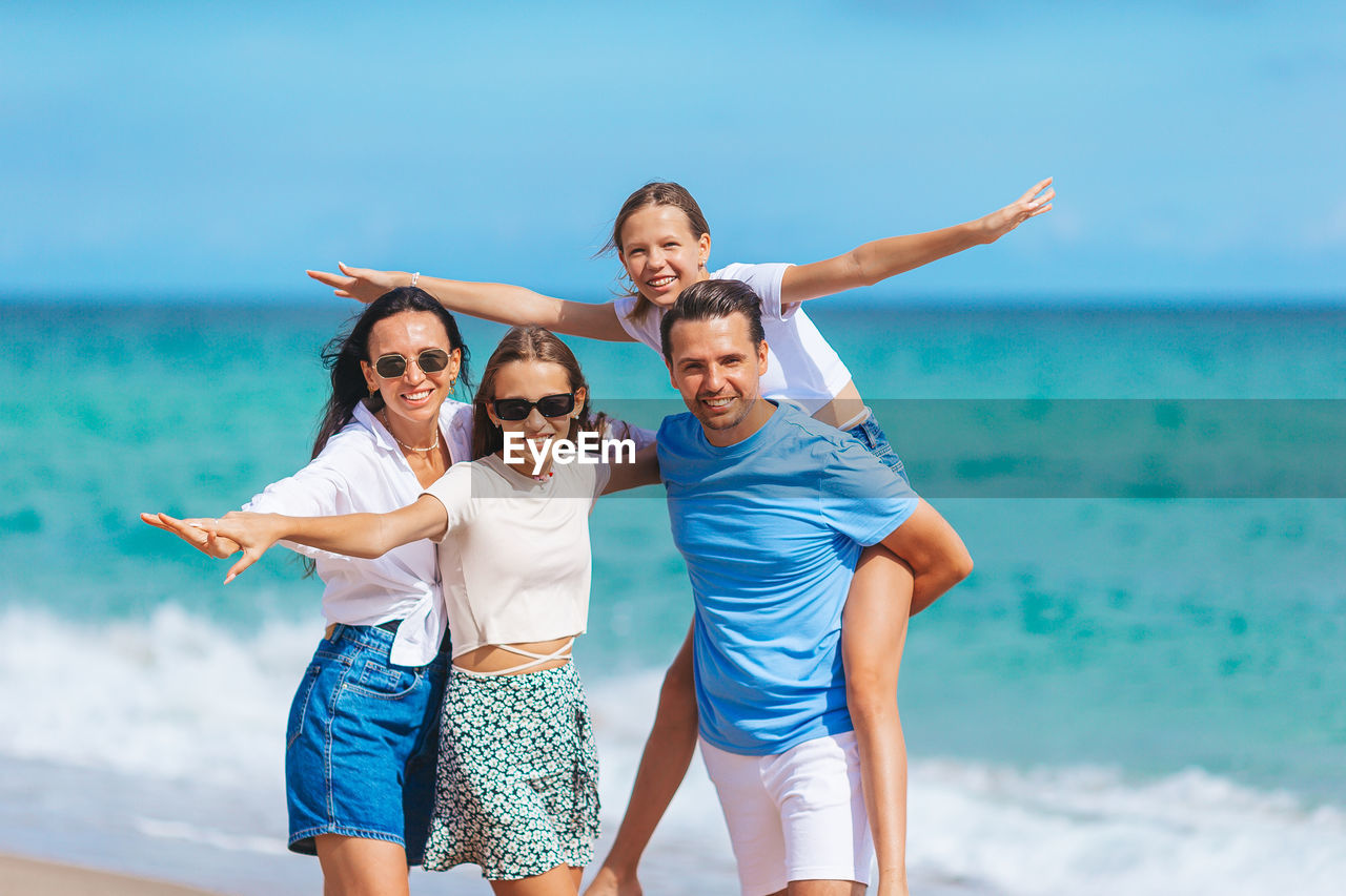 smiling friends standing against sea