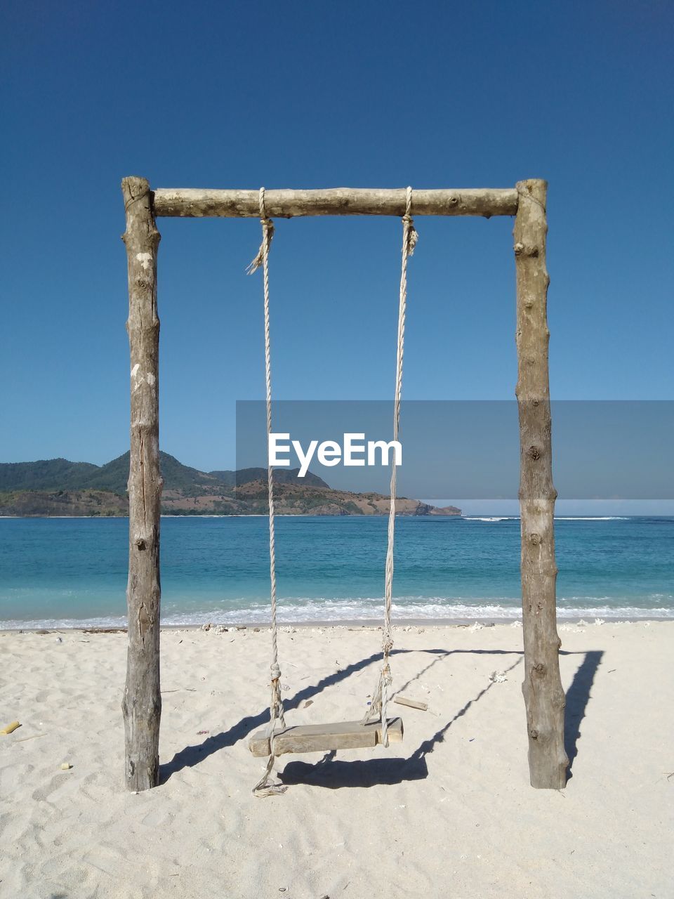 Wooden swing on beach against clear blue sky