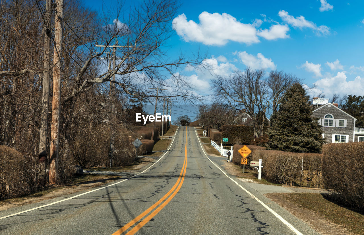 tree, road, transportation, sky, the way forward, plant, nature, sign, bare tree, symbol, cloud, architecture, city, day, street, road marking, diminishing perspective, marking, built structure, road sign, no people, rural area, mode of transportation, lane, vanishing point, autumn, outdoors, building exterior, transport, winter, infrastructure, travel