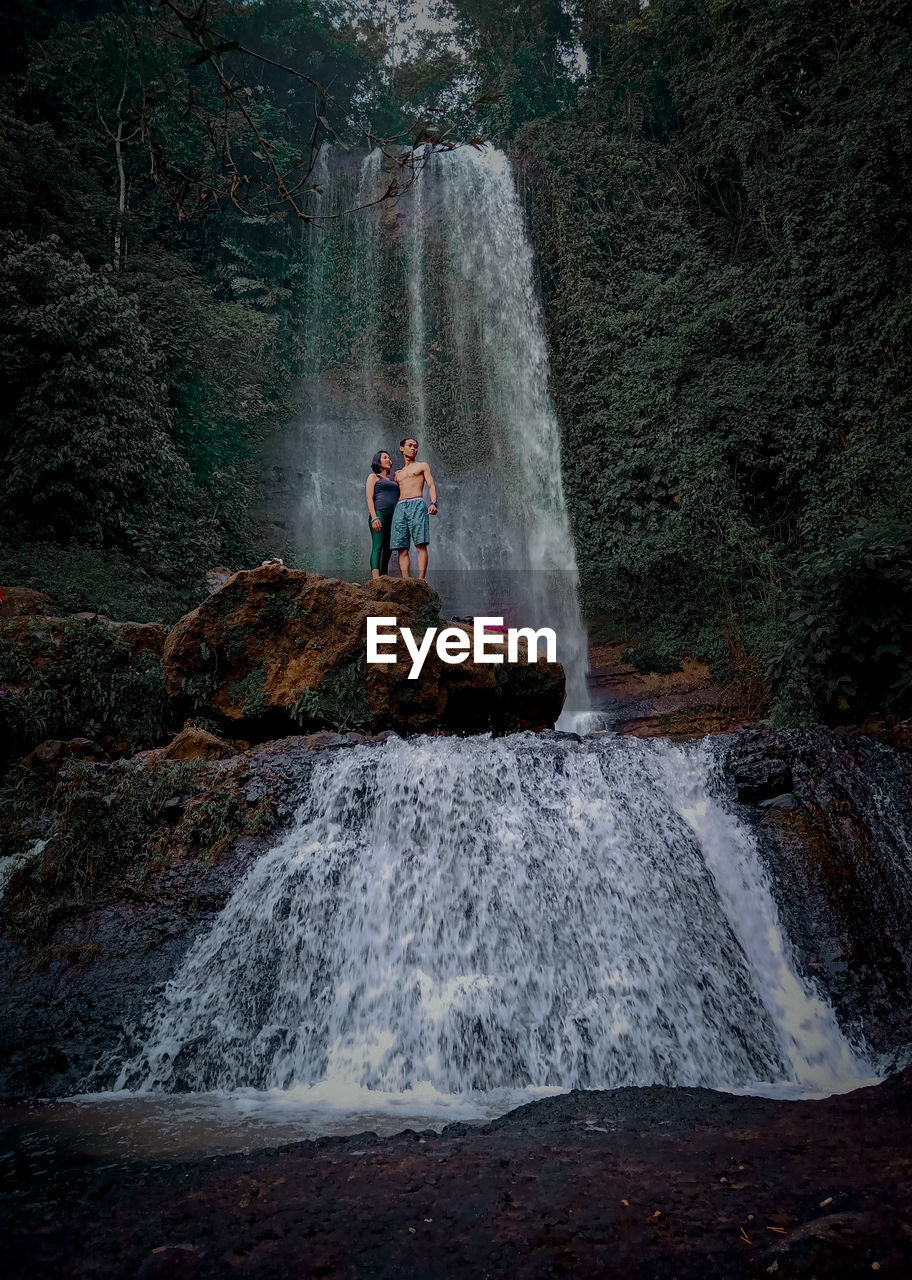 Couple standing on rock against waterfall in forest