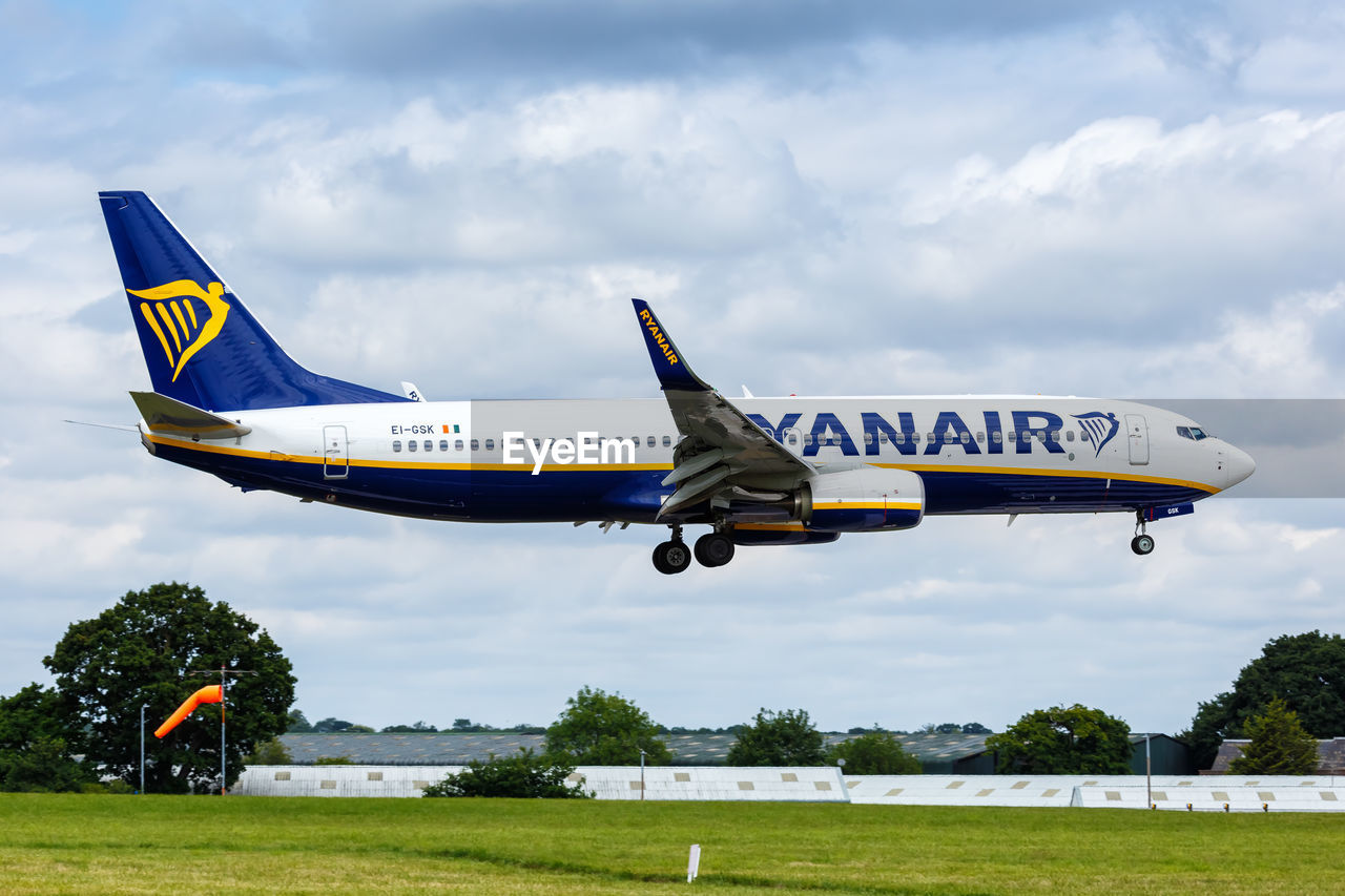 VIEW OF AIRPLANE FLYING OVER AIRPORT RUNWAY AGAINST SKY