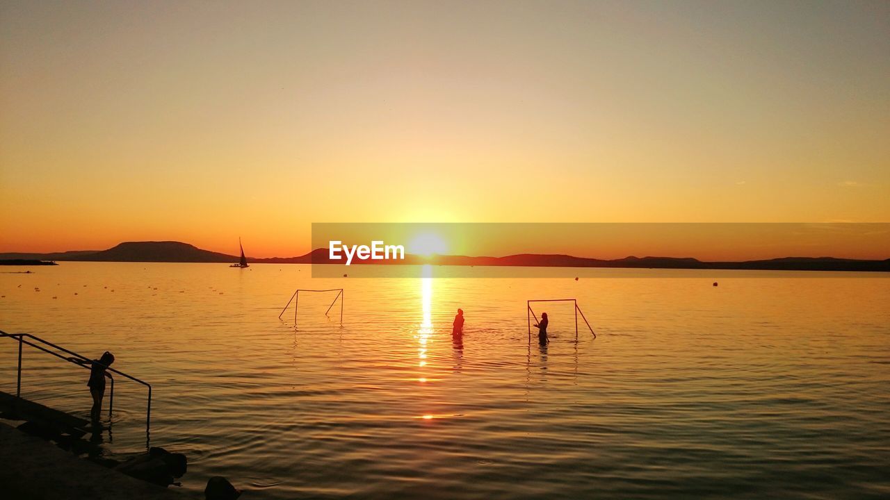 Silhouette man in sea against clear sky during sunset