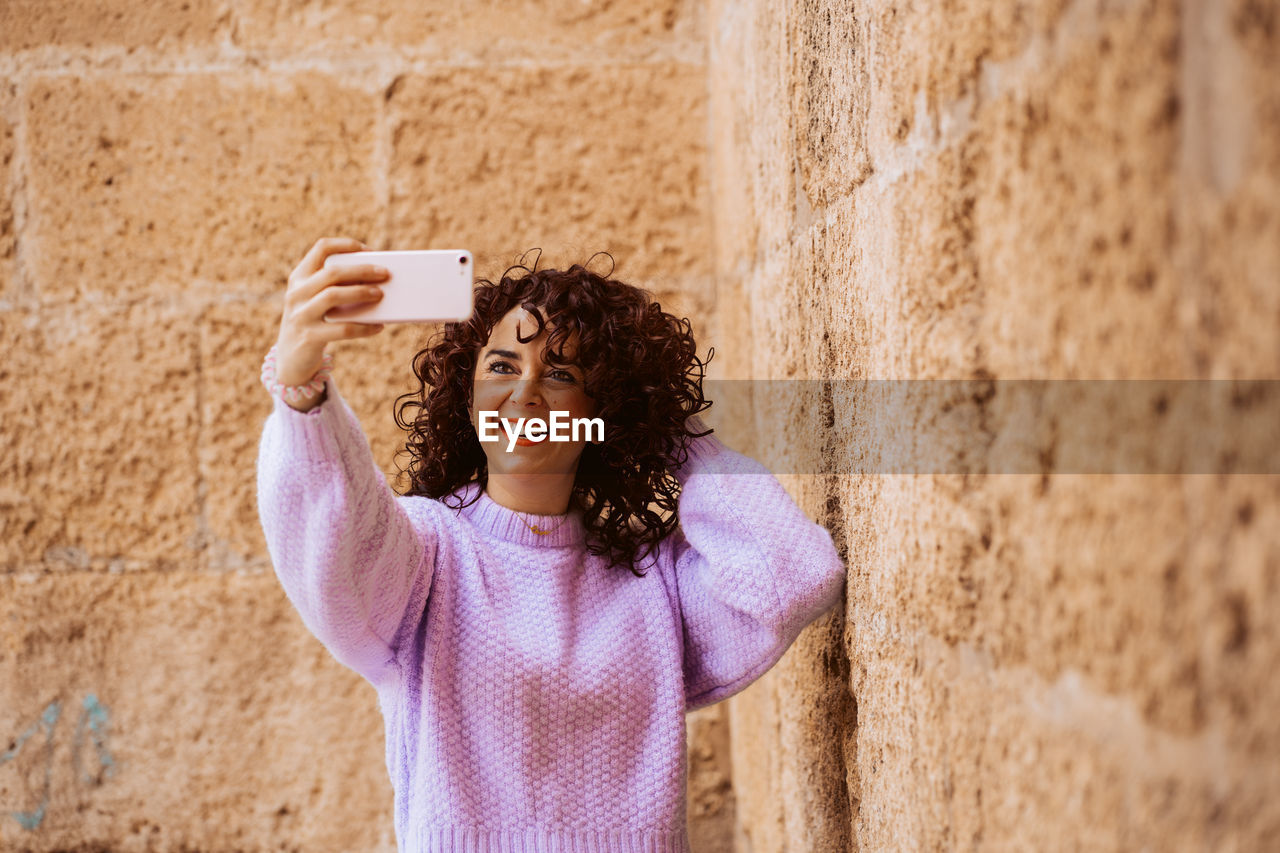 young woman using mobile phone while standing against wall