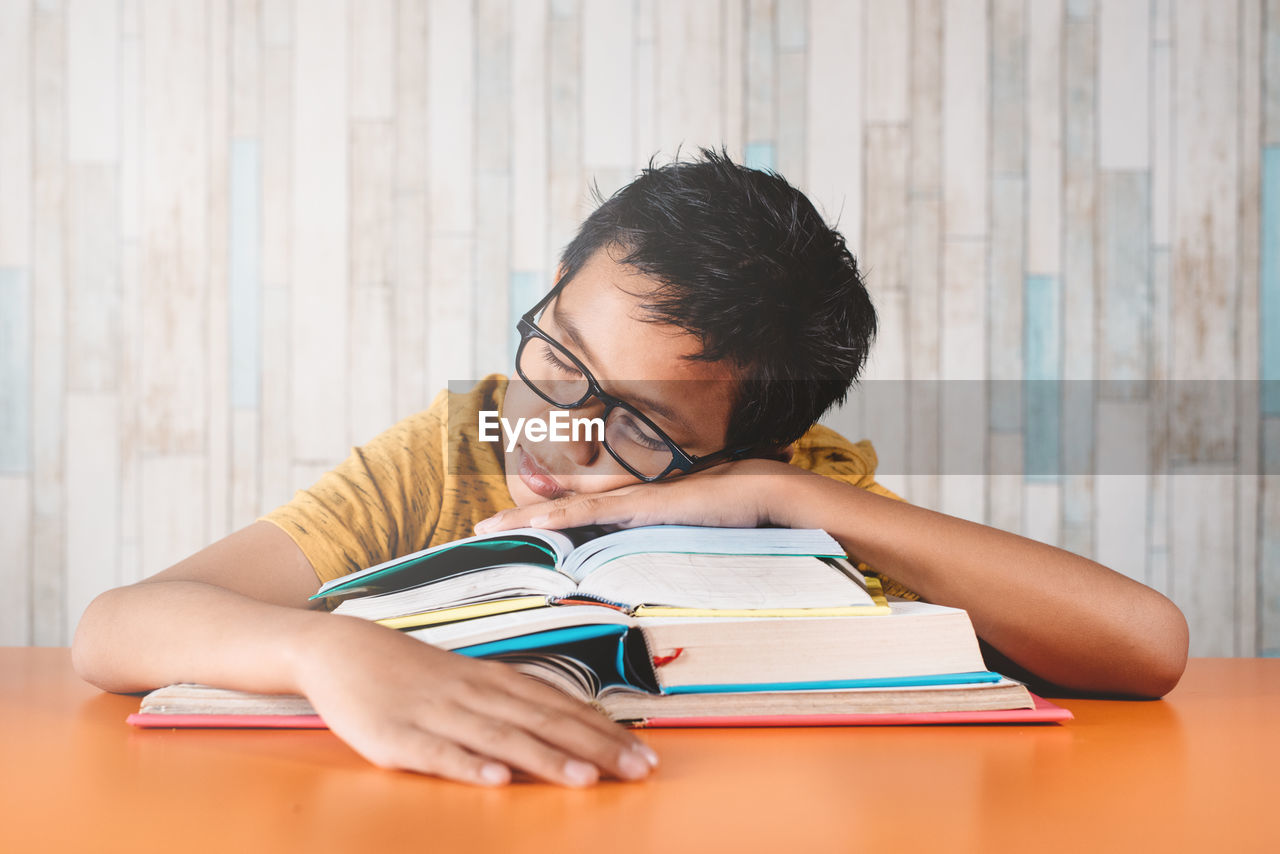 Young asian male student fall asleep on a stack of books while studying.