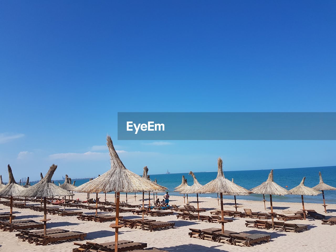 Chairs and thatched roofs at beach against blue sky