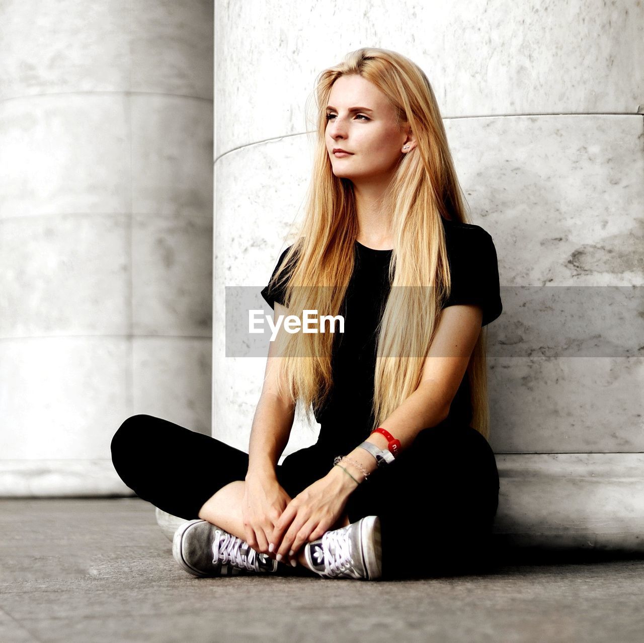 BEAUTIFUL YOUNG WOMAN SITTING AGAINST WALL IN BUILDING