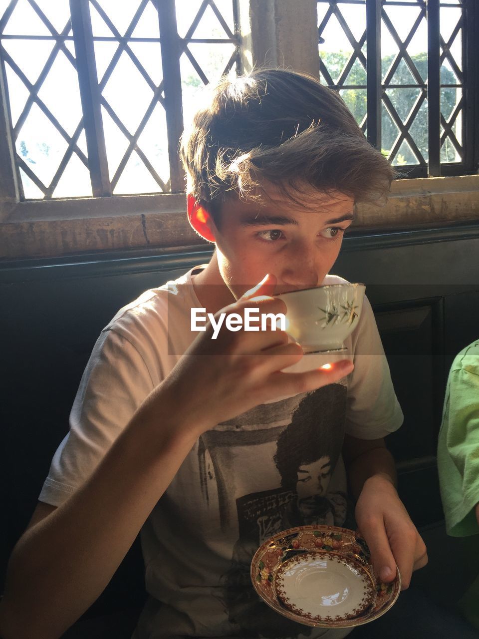 Boy drinking tea against window at home