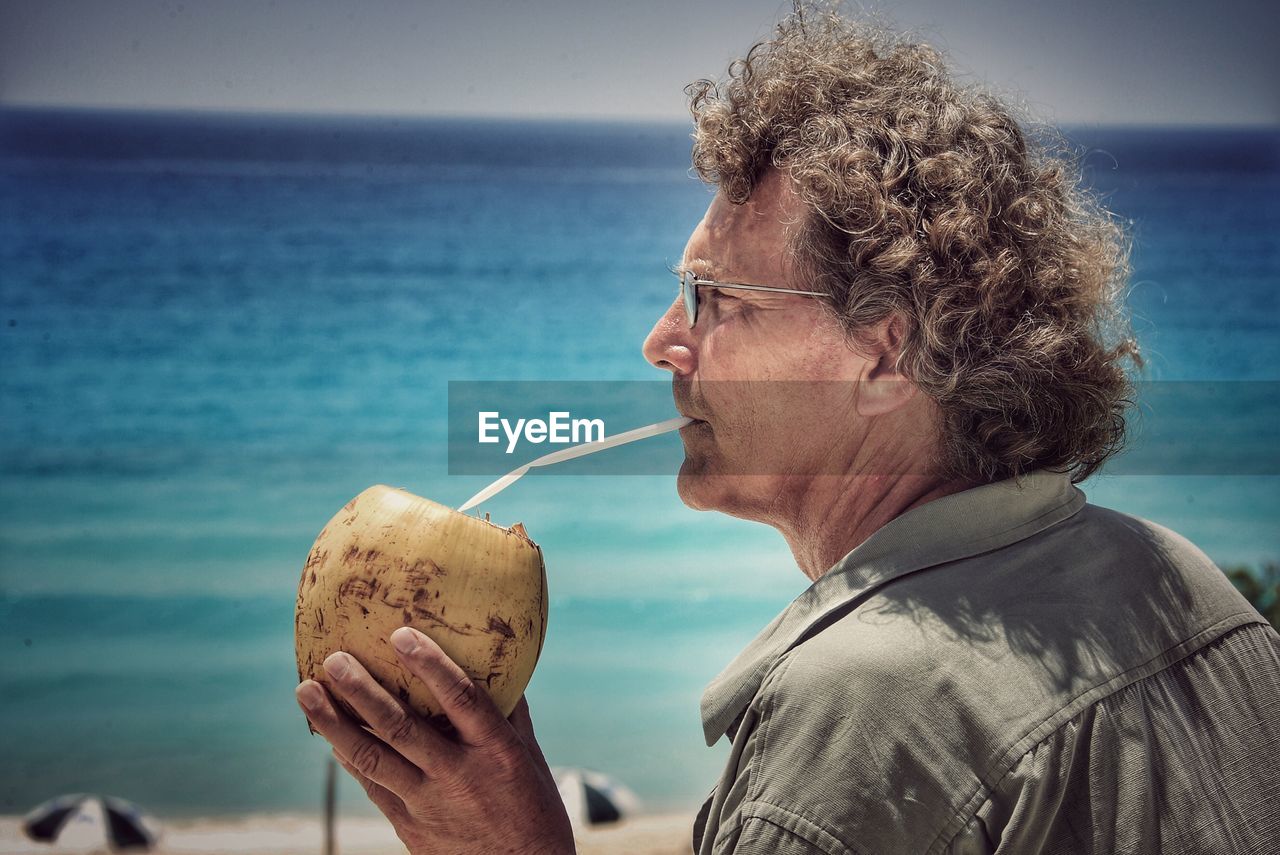Mature man drinking coconut water against sea