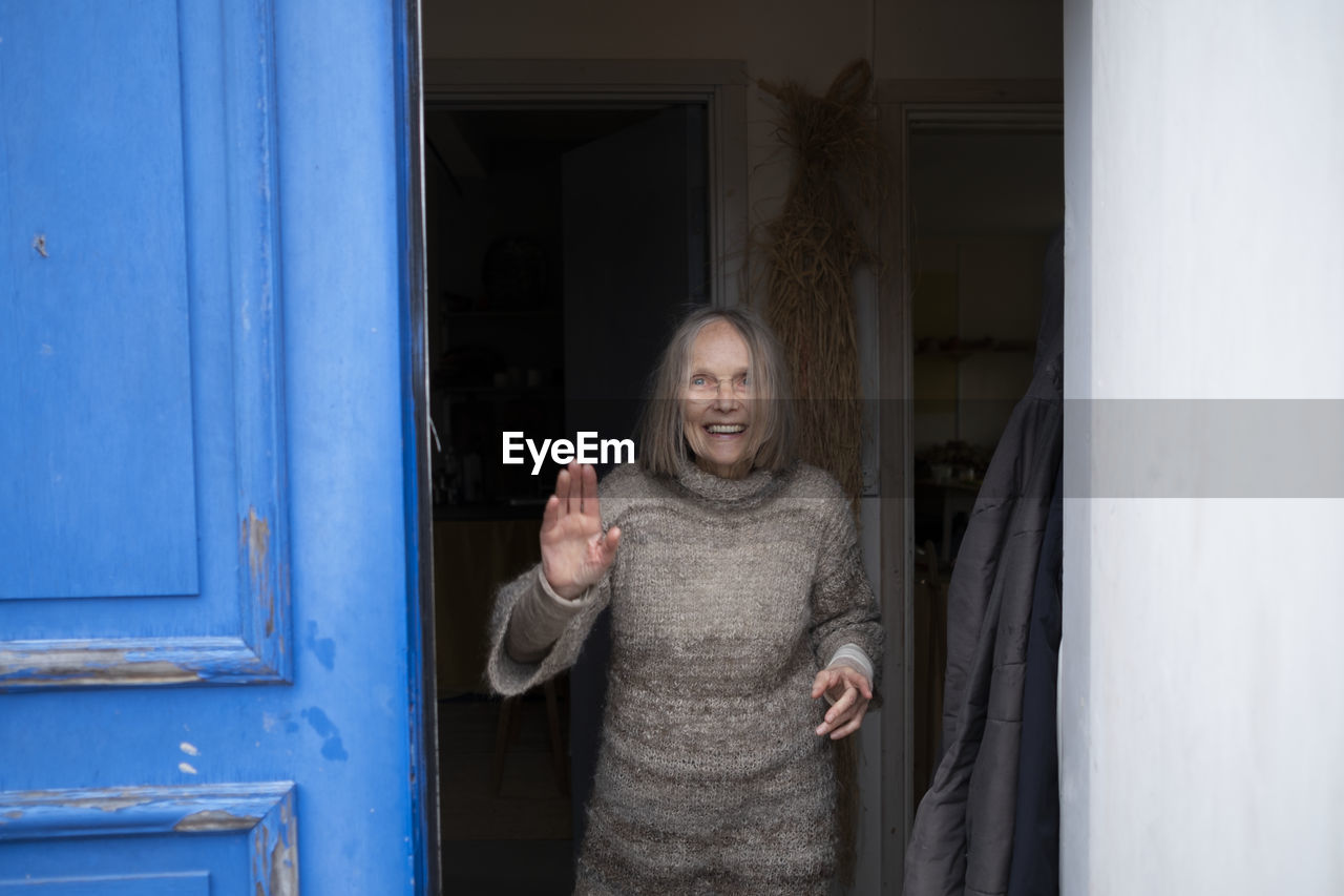 Smiling senior woman standing in doorway and waving