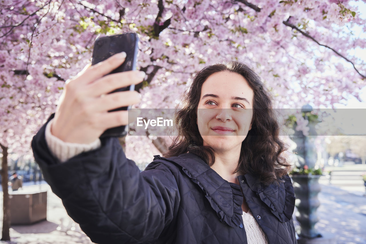 Young woman taking selfie against cherry trees