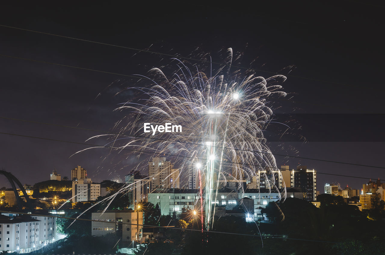 FIREWORK DISPLAY OVER ILLUMINATED BUILDINGS IN CITY AGAINST SKY