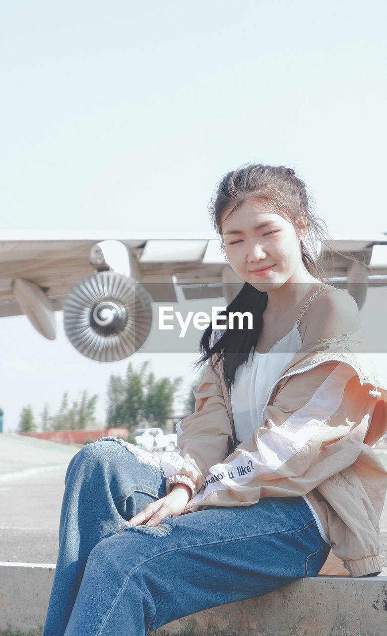 Portrait of smiling young woman sitting against sky