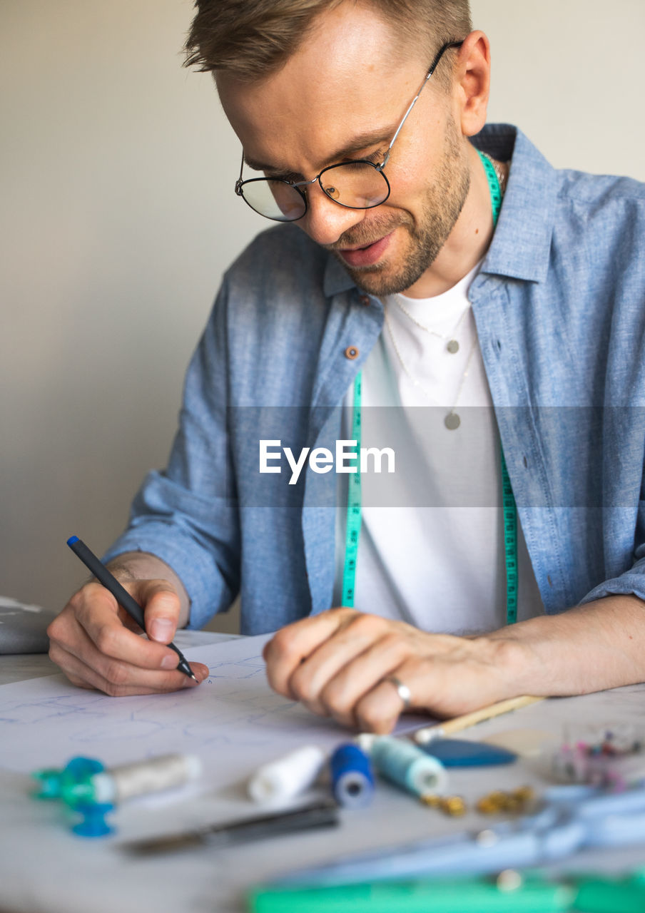 A diy designer draws a sketch. a smiling man in a blue shirt makes a sketch for sewing clothes