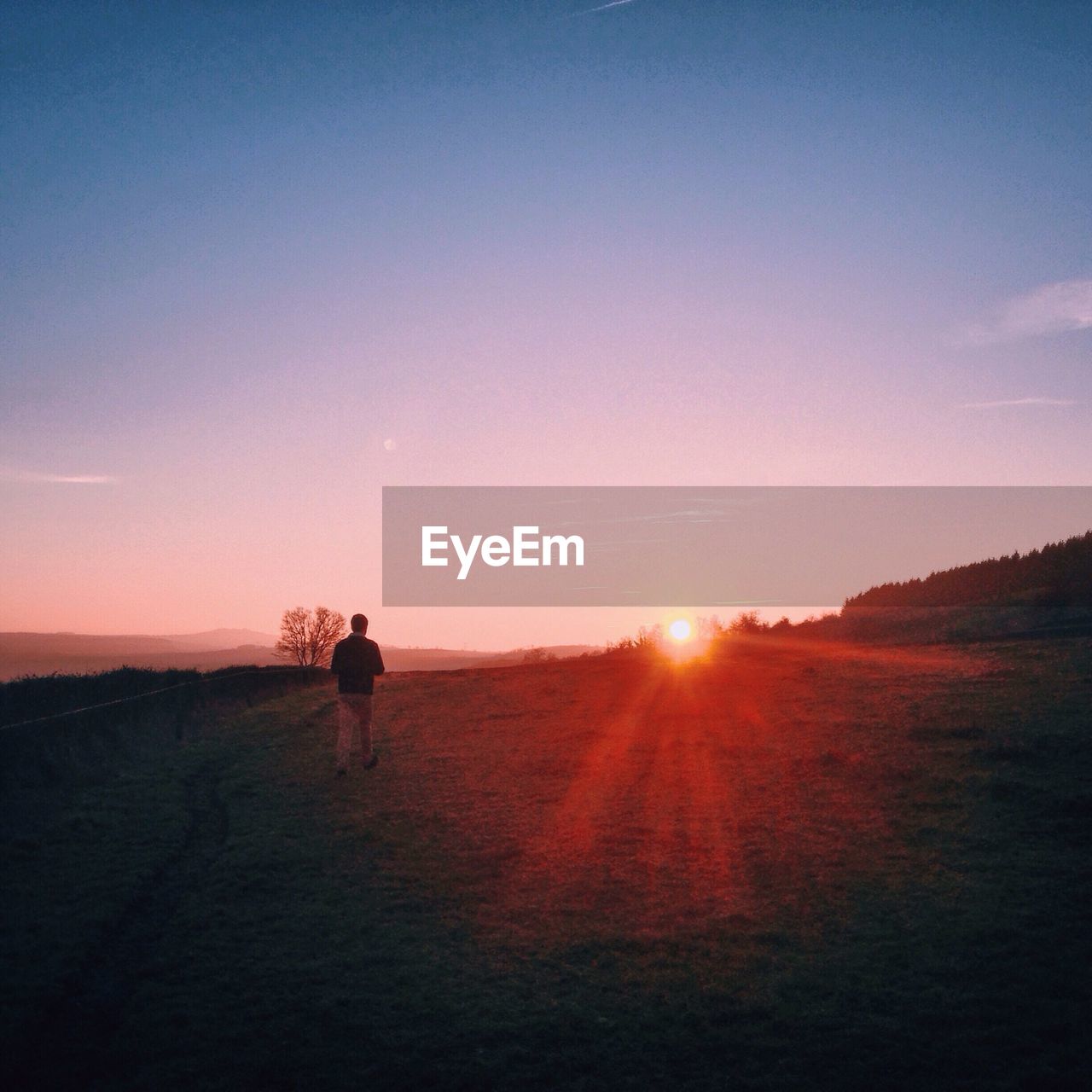 Rear view of man walking on landscape against sky during sunset