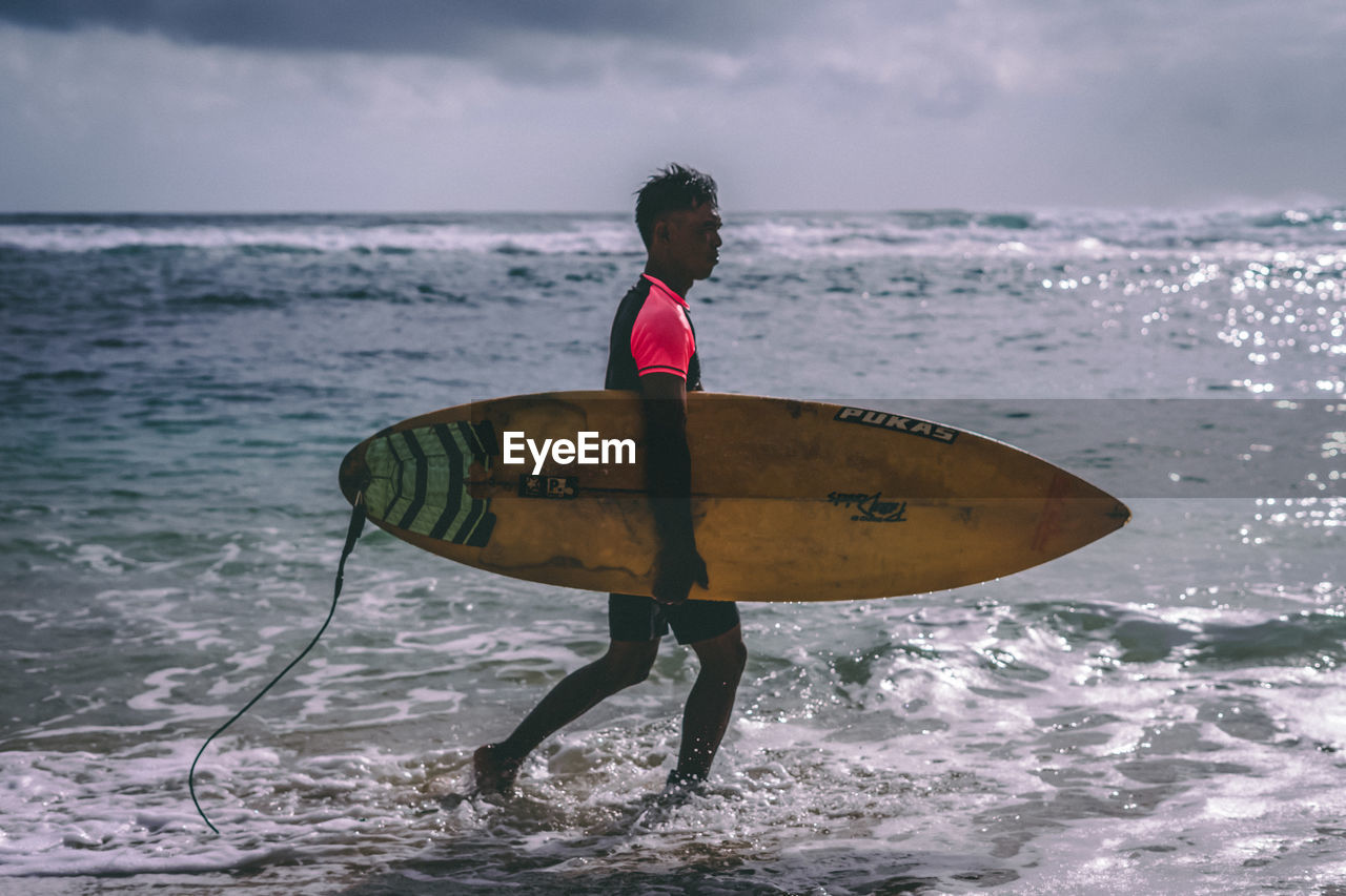 REAR VIEW OF MAN SURFING IN SEA