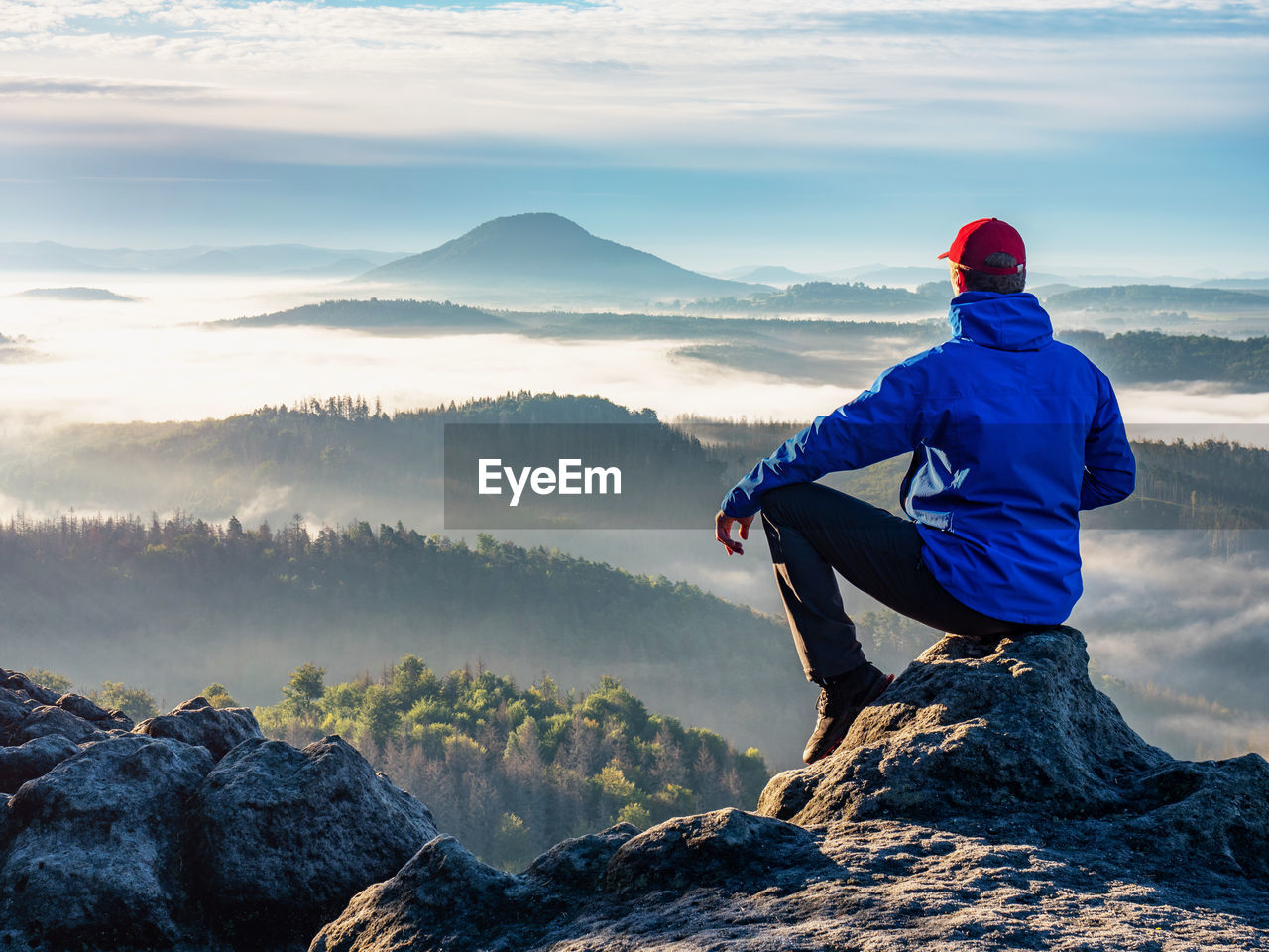 Man on the peak of rock. man sit with hand on knee with beautiful sunrise landscape. hiker is watch