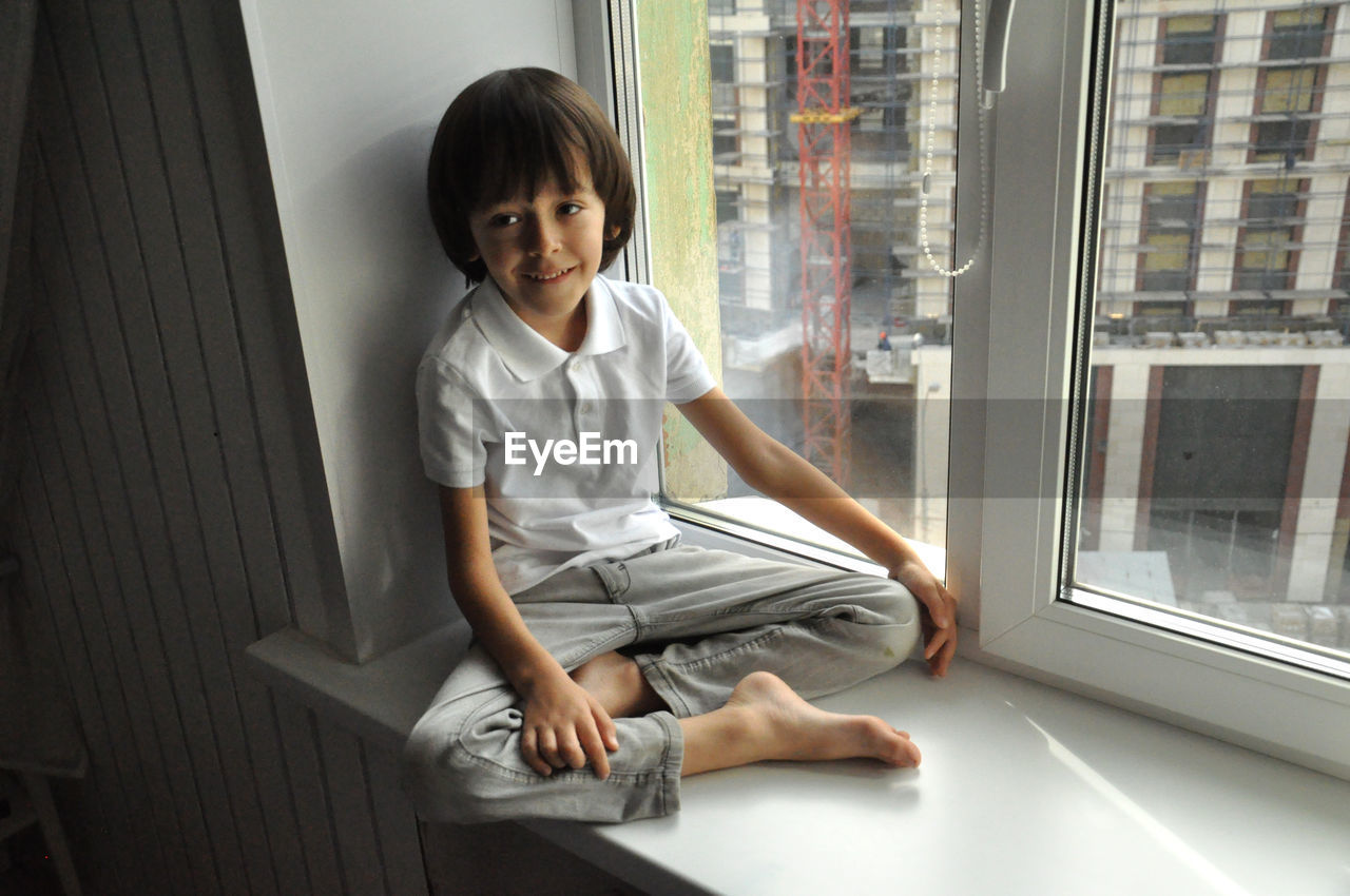 Brown haired boy sitting at windowsill and looking on street