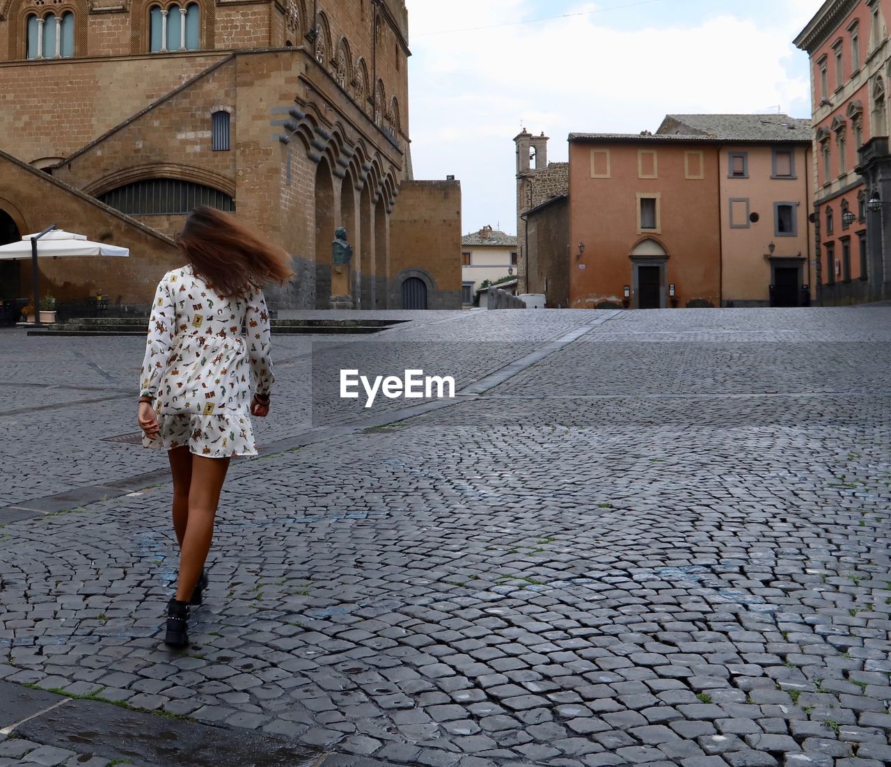 FULL LENGTH REAR VIEW OF WOMAN WALKING ON STREET AGAINST BUILDINGS