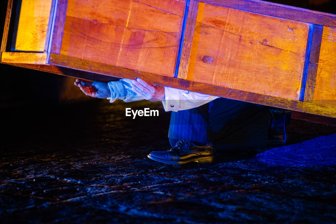 Low section of man holding cabinet on road at night