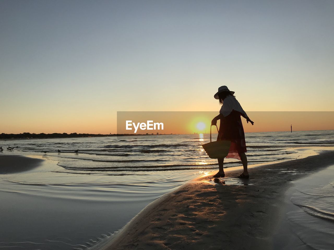 Silhouette woman standing on beach against sky during sunset