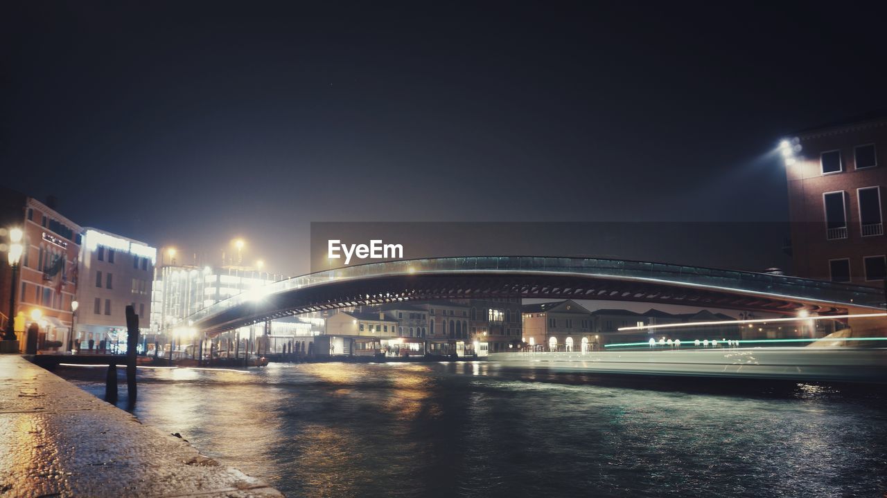 ILLUMINATED BRIDGE OVER RIVER AT NIGHT