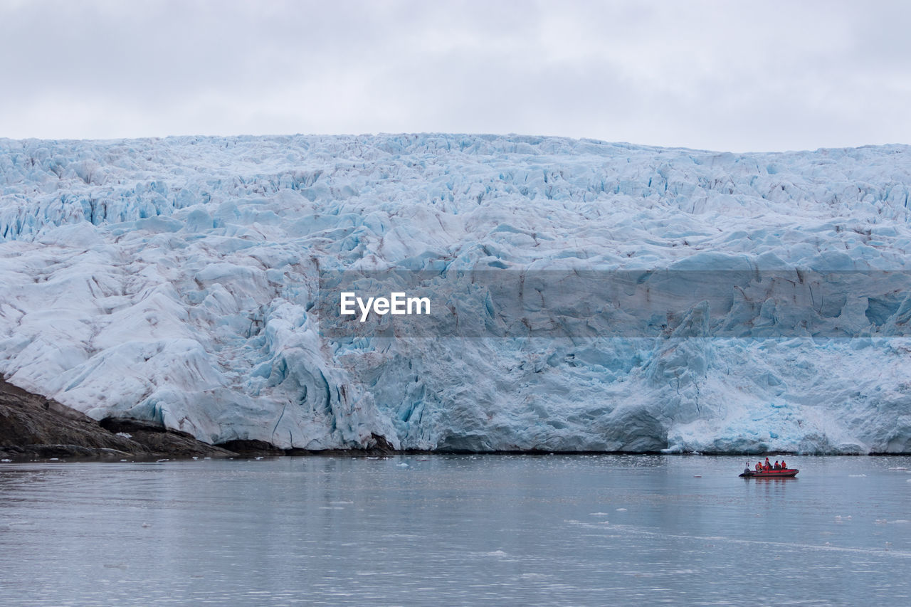 Unidentified tourists on a speedboat admiring large glacier from a close distance in svalbard