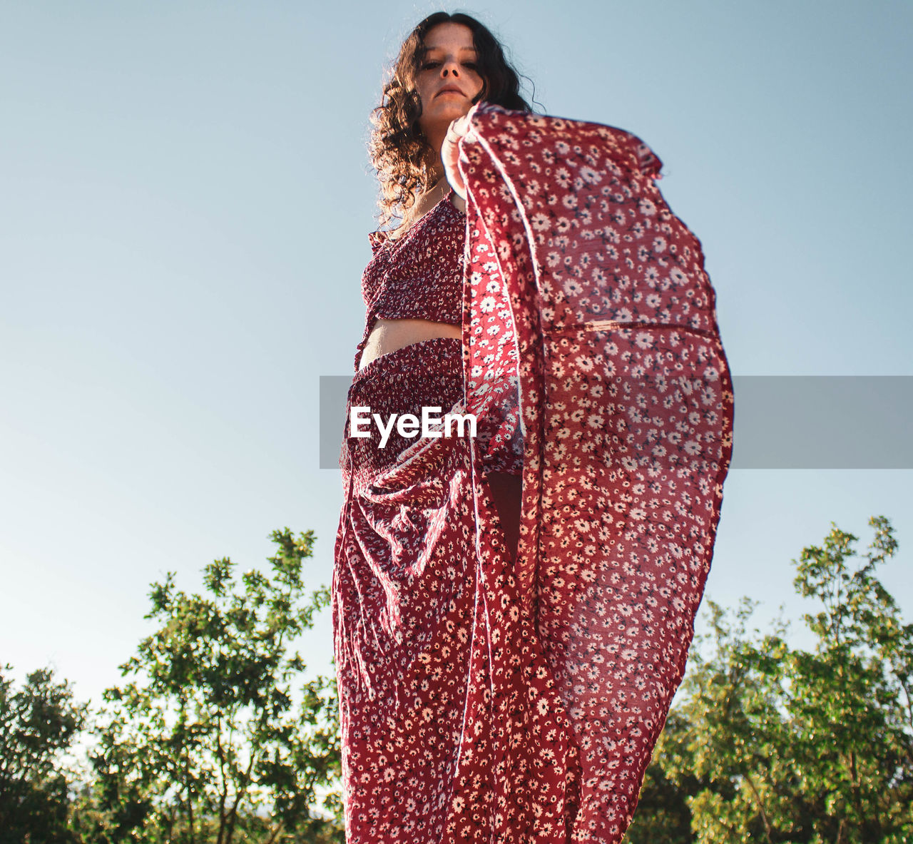 Young girl in long red summer dress on the fly agaisnt blue sky