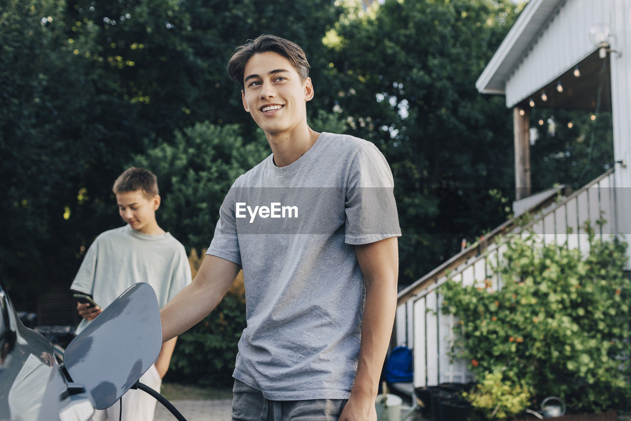 Smiling young man charging electric car in back yard