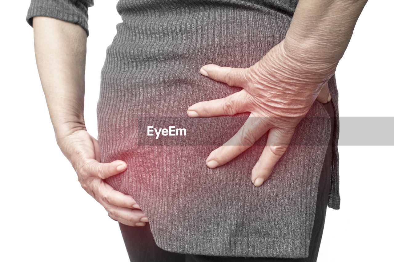 Midsection of woman massaging buttocks against white background