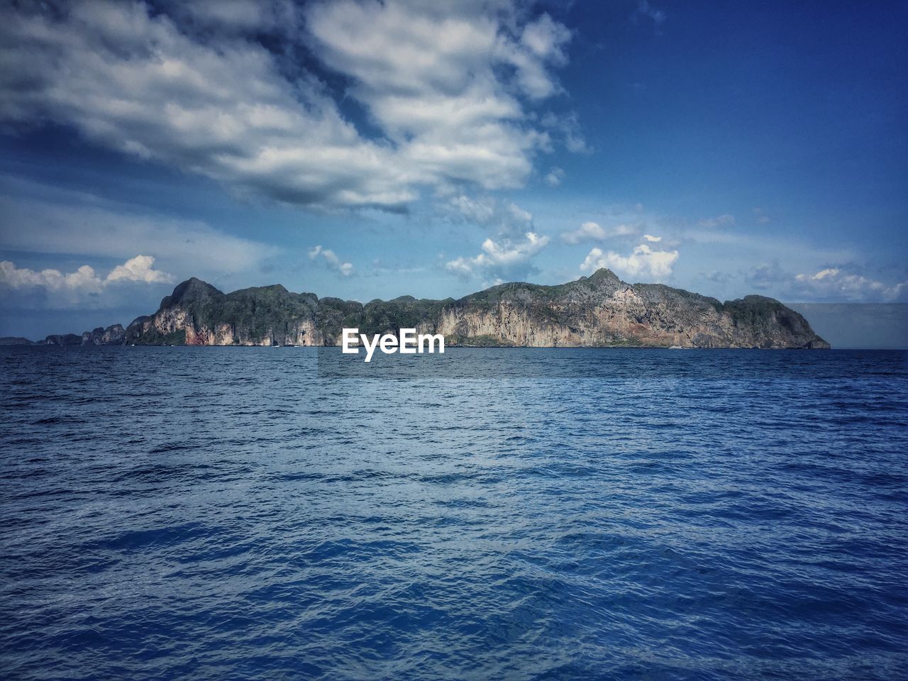 Scenic view of sea against sky with small rock formation on horizon