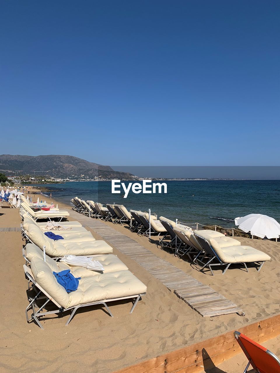 Deck chairs on beach against clear blue sky