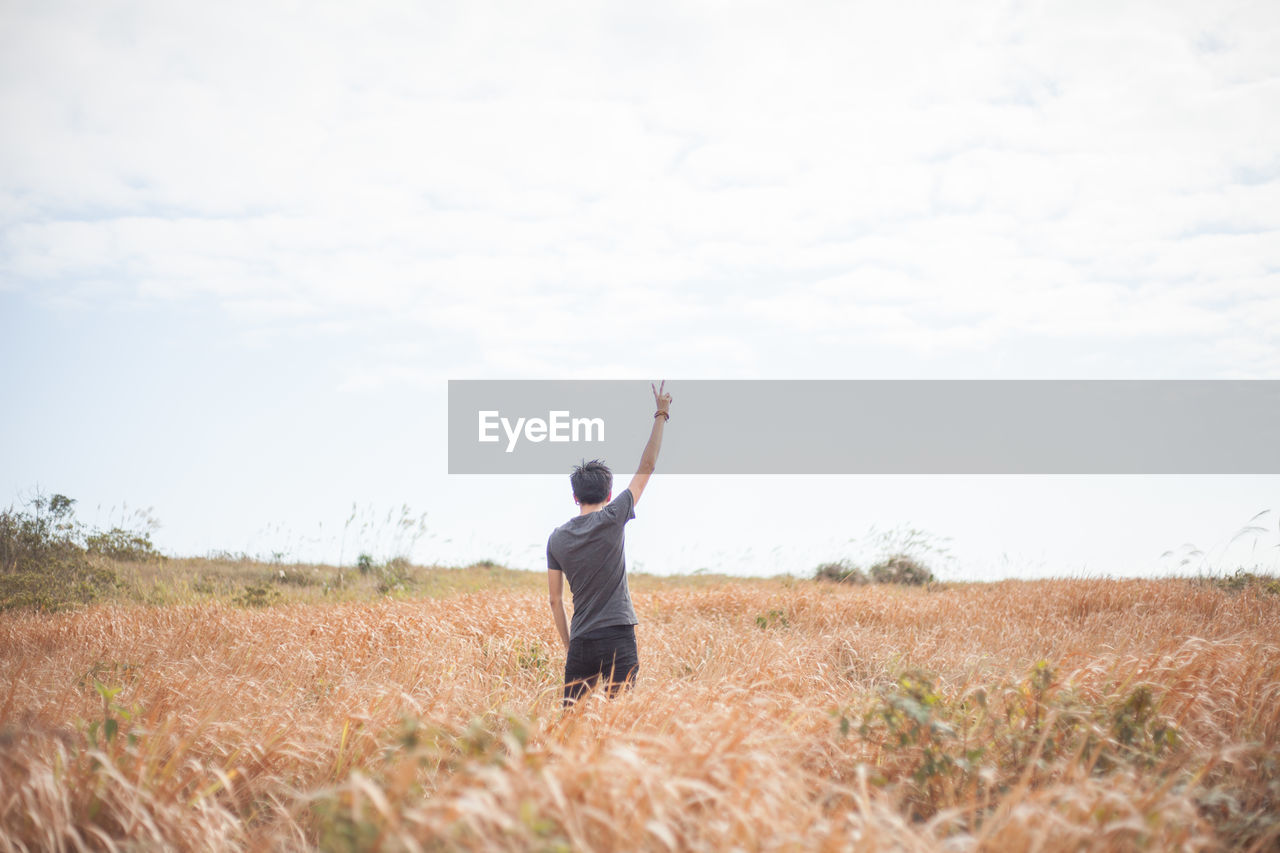 Rear view of man gesturing peace sign on agricultural field against sky