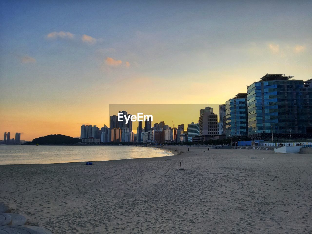 Sea by city buildings against sky during sunset