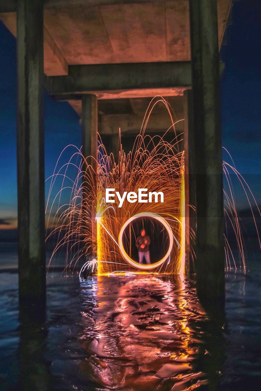 ILLUMINATED FERRIS WHEEL BY WATER AT NIGHT