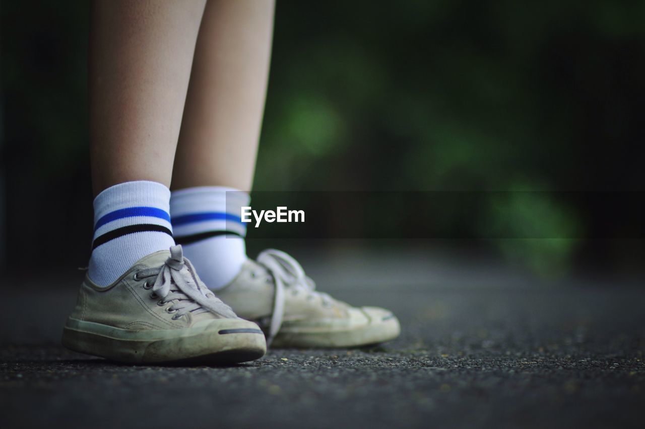 Low section of person wearing canvas shoes while standing on walkway