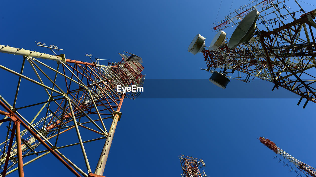 Low angle view of television towers against clear blue sky during sunny day