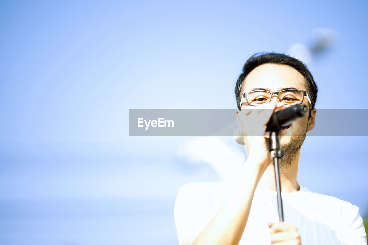 Close-up of man singing while standing against blue sky